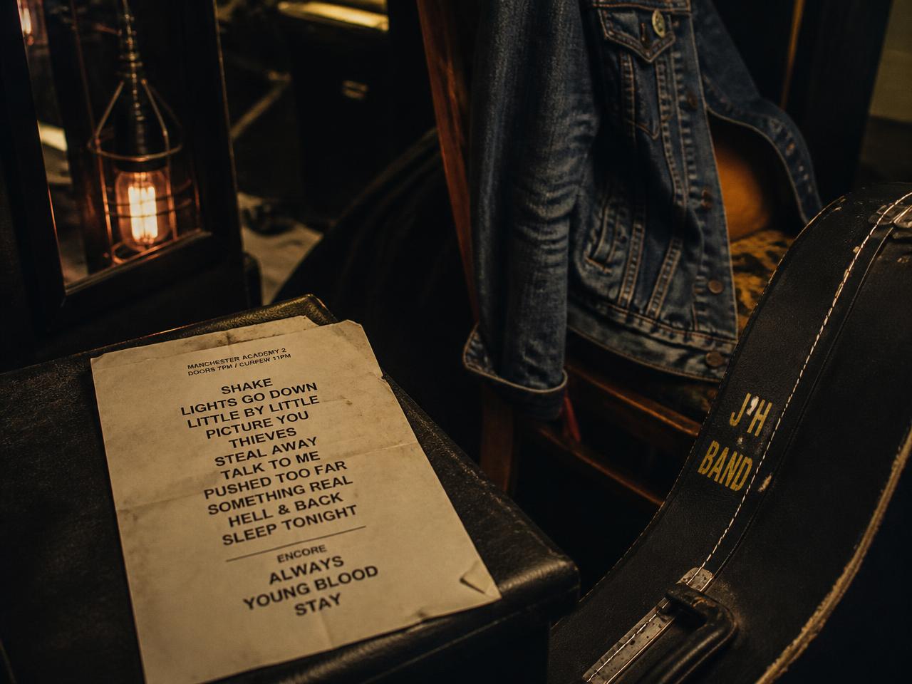 A worn handwritten setlist beside a guitar case and denim jacket backstage before doors open